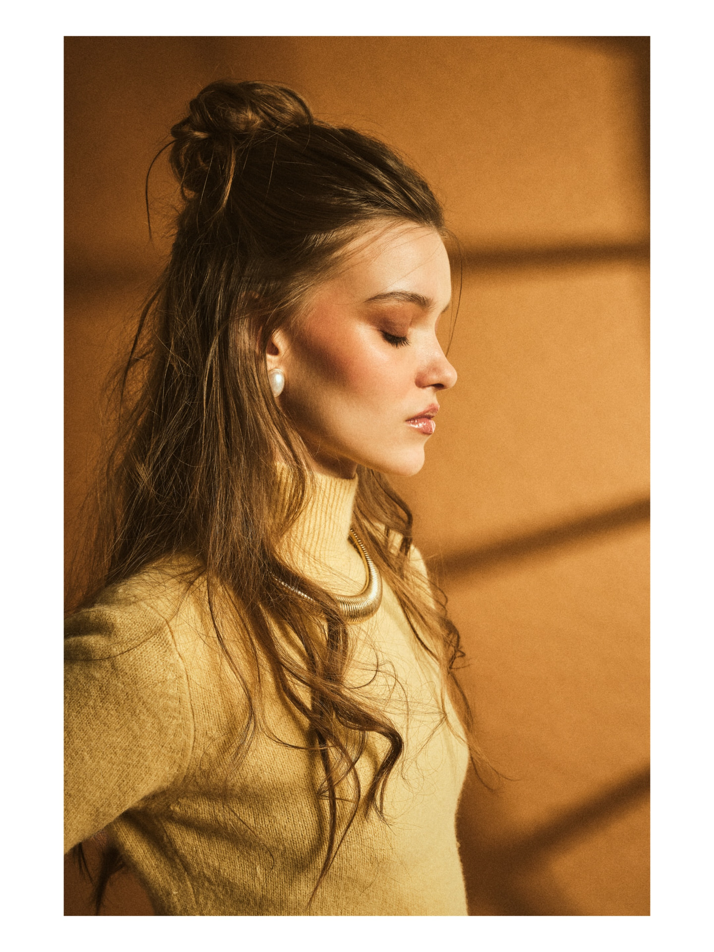 Studio portrait in warm light with a soft yellow knit and gold collar necklace
